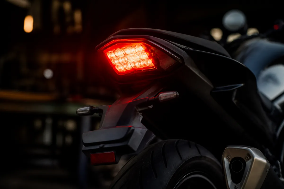 Motard vérifiant l’éclairage arrière de sa moto dans un garage avant un contrôle technique