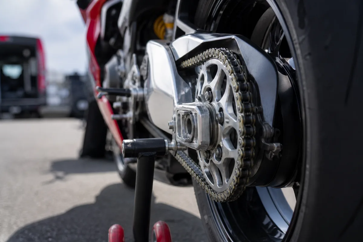 Chaîne et couronne d’une moto sportive photographiées de près sur une béquille de stand dans un paddock