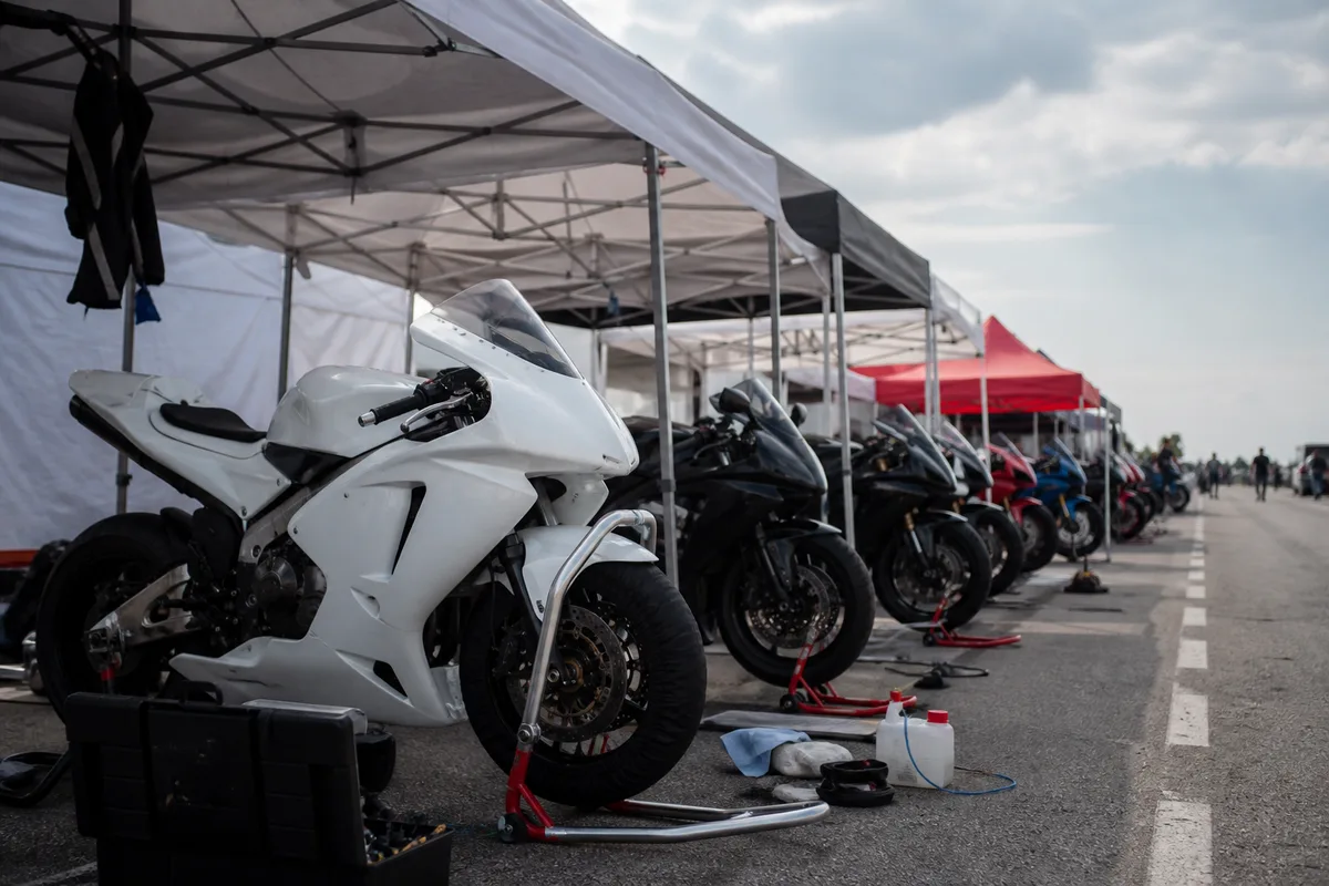 Paddock de circuit avec motos alignées sous des tentes, caisses à outils et béquilles de stand