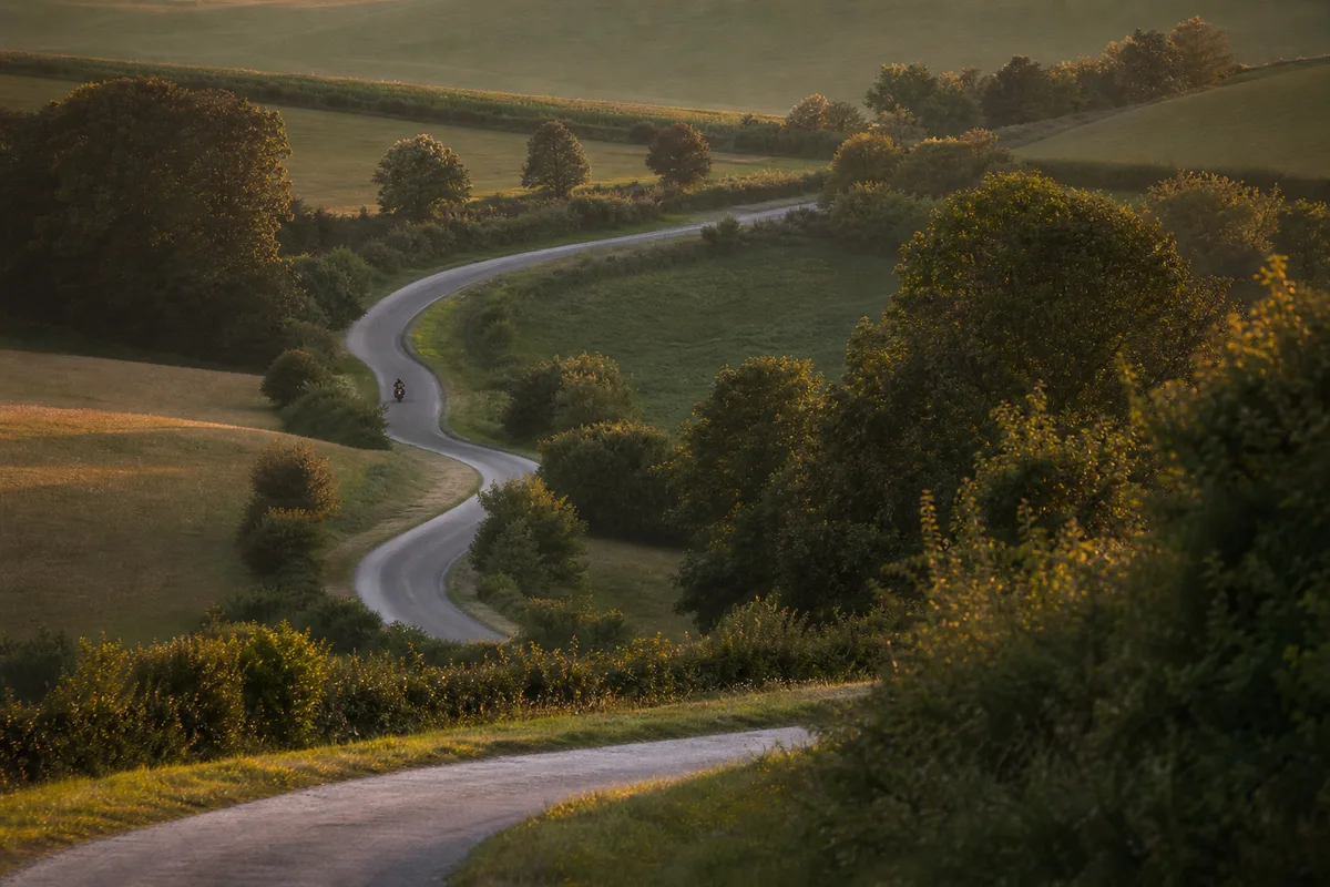 Route départementale sinueuse traversant une campagne française vallonnée en fin de journée