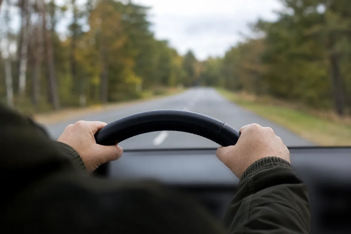 Mains d’un conducteur posées sur le volant d’une voiture sur une route de campagne
